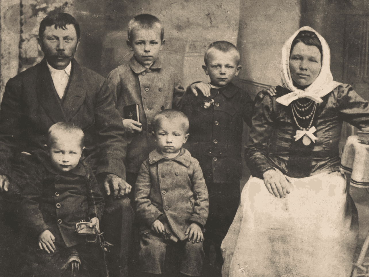 Rodzina wielodzietna w miejscowości na Kresach Wschodnich. Ojciec i matka w otoczeniu czterech kilkuletnich synów. Odświętnie ubrani w strojach charakterystycznych dla początku XX wieku. Jeden z chłopców trzyma modlitewnik. Link do strony z artykułem zainspirowanym Zbiorami Społecznymi