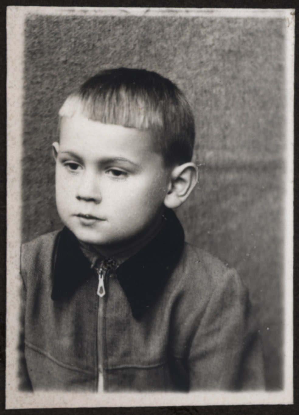 Czarno-biały portret małego dziecka ubranego w kurtkę z ciemnym kołnierzem, patrzącego lekko w bok na jednolitym tle.