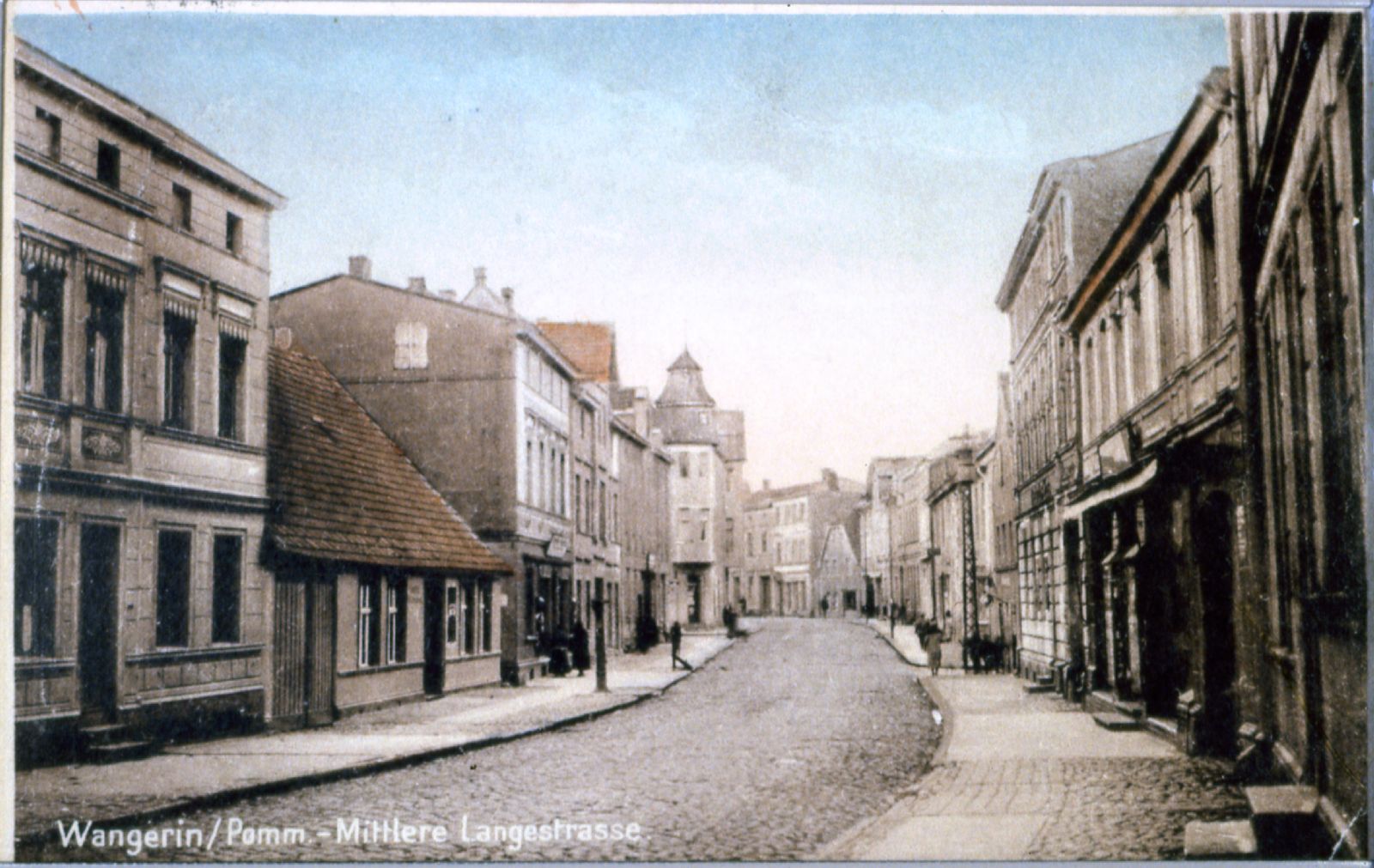 Widok historycznej pocztówki przedstawiającej brukowaną ulicę wyłożoną budynkami w Wangerin na Pomorzu; podpis brzmi: "Wangerin/Pomm. Mittlere Langestrasse.