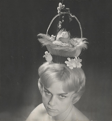 Głowa modelki prezentującej fantazyjną fryzurę. Włosy uformowane są w wielkanocny koszyczek z kurczakami i baziami. Link do podstrony z tym zdjęciem