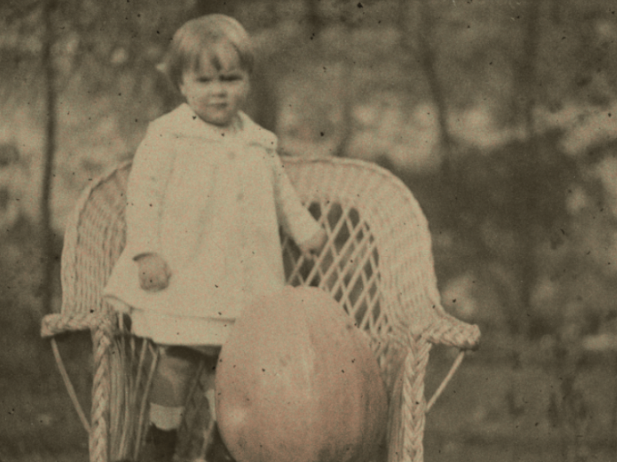 Dziecko siedzi na wiklinowym krześle z dynią.