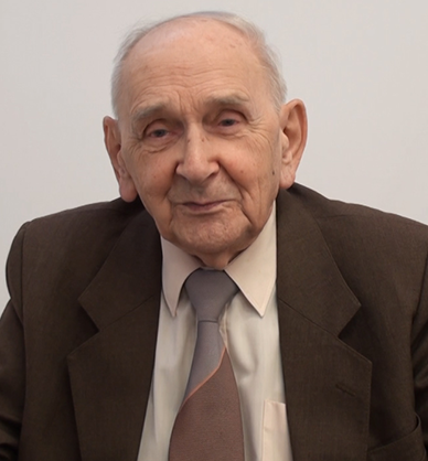 Starszy mężczyzna w marynarce, jasnej koszuli i krawacie. Delikatnie się uśmiecha. Link do podstrony z tym nagraniem wideo