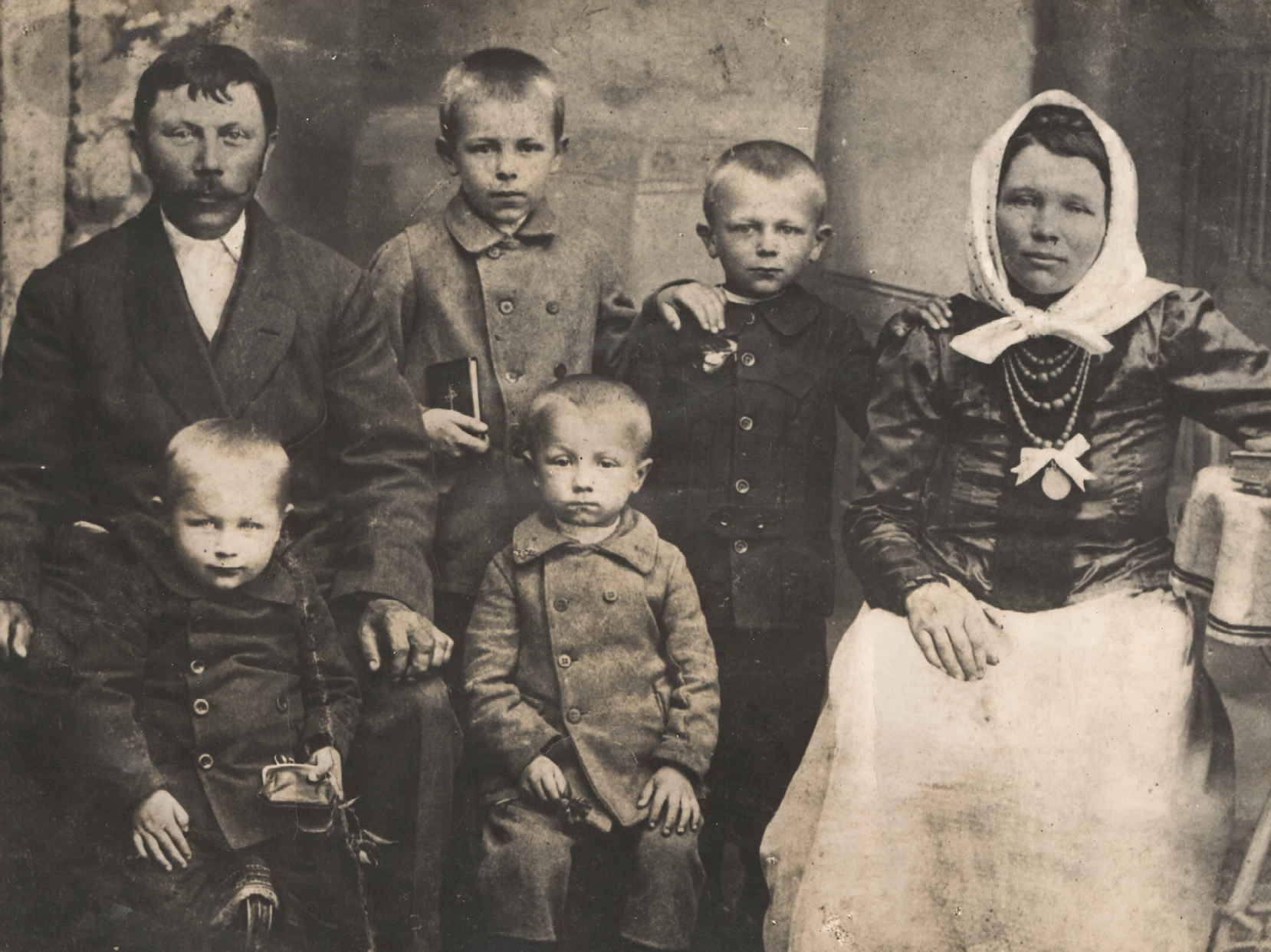 Rodzina wielodzietna w miejscowości na Kresach Wschodnich. Ojciec i matka w otoczeniu czterech kilkuletnich synów. Odświętnie ubrani w strojach charakterystycznych dla początku XX wieku. Jeden z chłopców trzyma modlitewnik. Link do strony z artykułem zainspirowanym Zbiorami Społecznymi